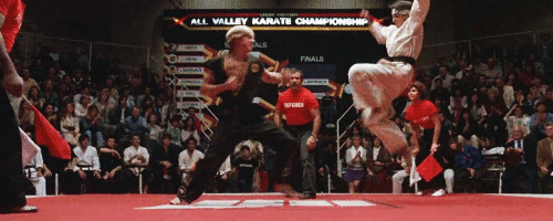 A fighter in black being kicked in the face by a fighter in white